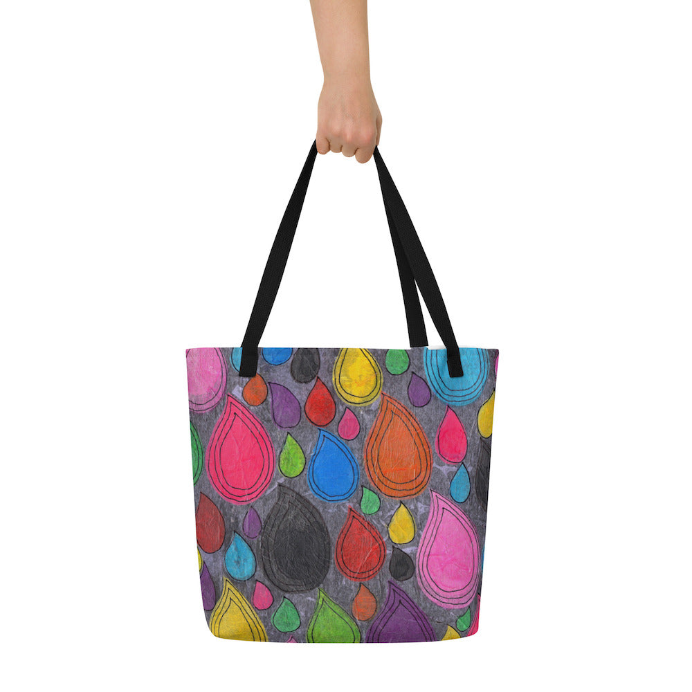Big sturdy graphic tote bag with multicolor Dripdrop print on front and black straps held by hand.