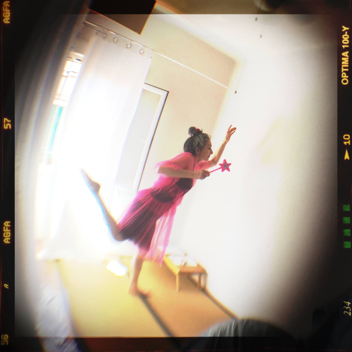 Quirky self portrait using fisheye lens of Alex Mitchell dressed in pink tulle dress holding magic wand and posing as pink fairy.