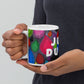 Colorful ceramic coffee mug with quirky slogan Just Ducky in white letters on Dripdrop design, hands holding left view.