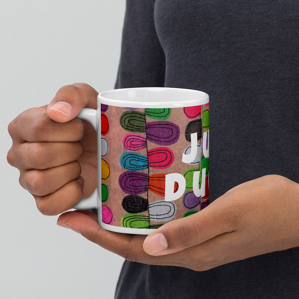 Colorful ceramic coffee mug with quirky slogan Just Ducky in white letters on Flipflop design, hands holding left view.