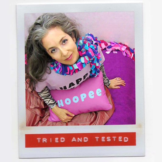 Alex Mitchell all dressed up in colorful setting feeling fab with her boa scarf and with Whoopee slogan pillow on her lap.