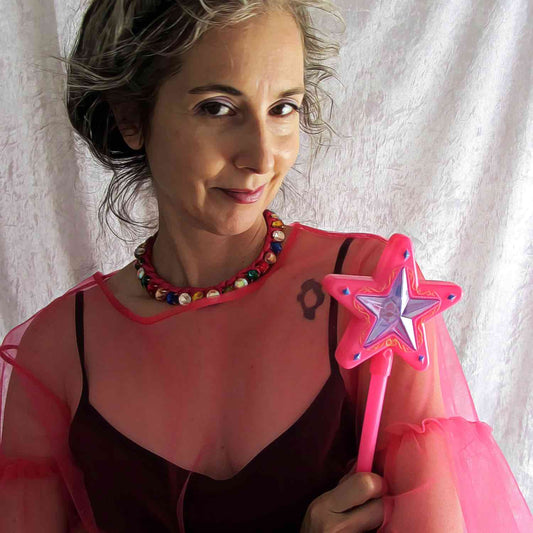 Funny self portrait of Alex Mitchell in pink tulle dress and magic fairy wand with her arms crossed and a knowing smile