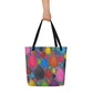 Big sturdy graphic tote bag with multicolor Dripdrop print on front and black straps held by hand.