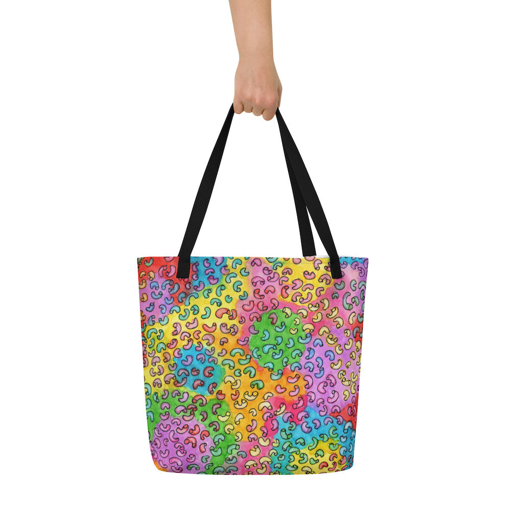 Big sturdy graphic tote bag with multicolor Macaroni print on front and black straps held by hand.