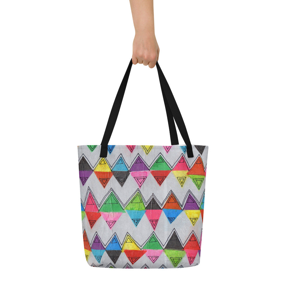 Big sturdy graphic tote bag with multicolor Zigzag print on front and black straps held by hand.