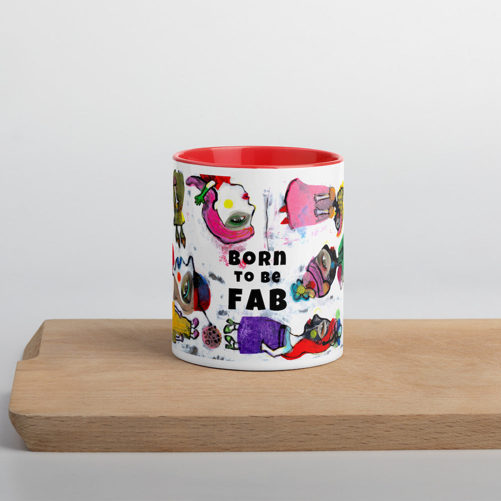 Graphic coffee mug with slogan Born To Be Fab and red accent color on rim and interior on wood counter front view.