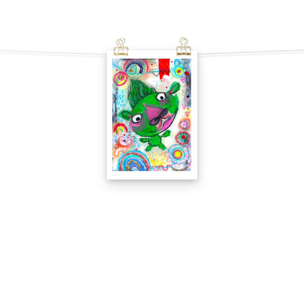 Colorful happy fine art print of a green monster smiling on vibrant background hanging on wall from a string with gold clips.