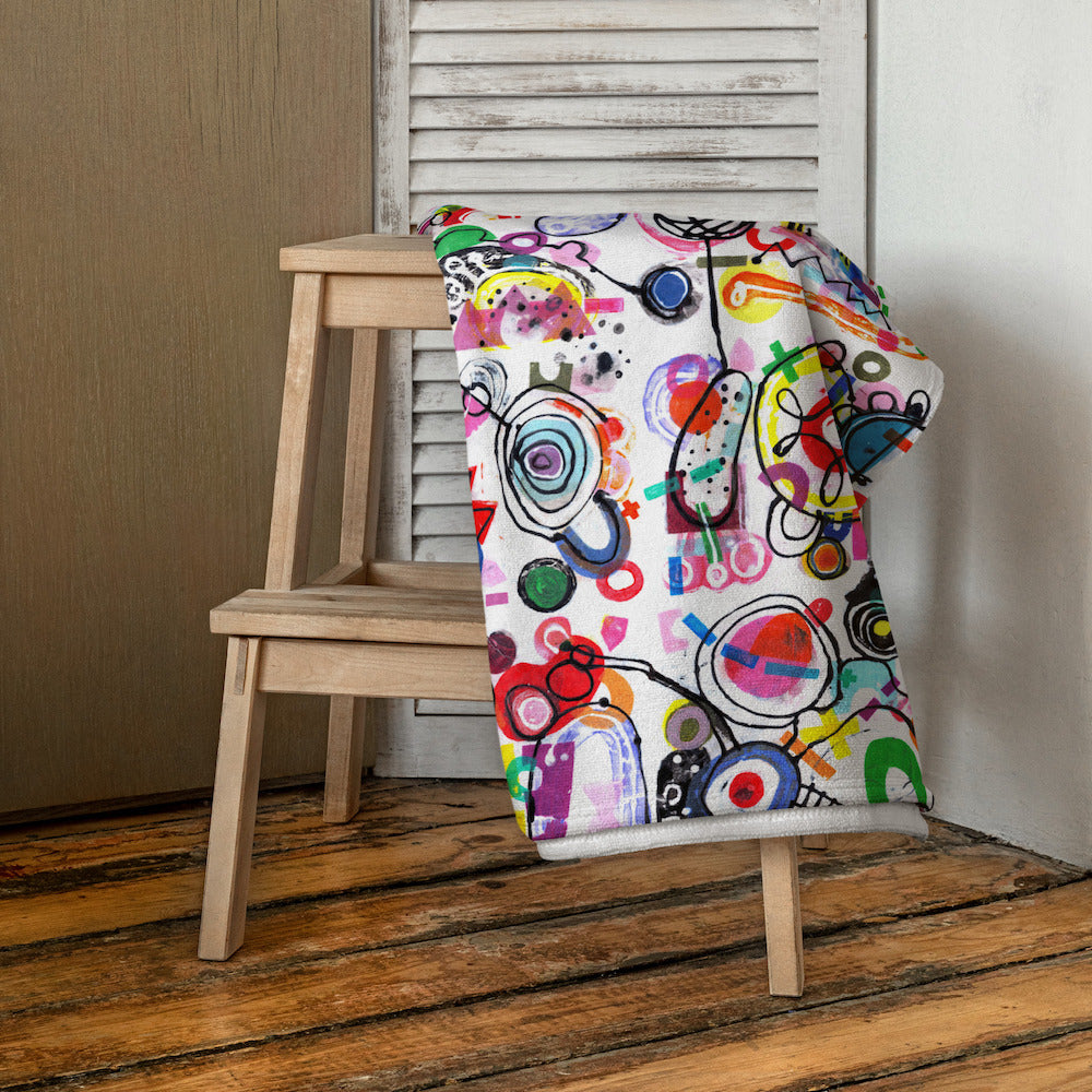 Stylish soft chic beach towel with bold multicolor Treasure Map print in cheerful and playful style. Folded and hanging on stool.