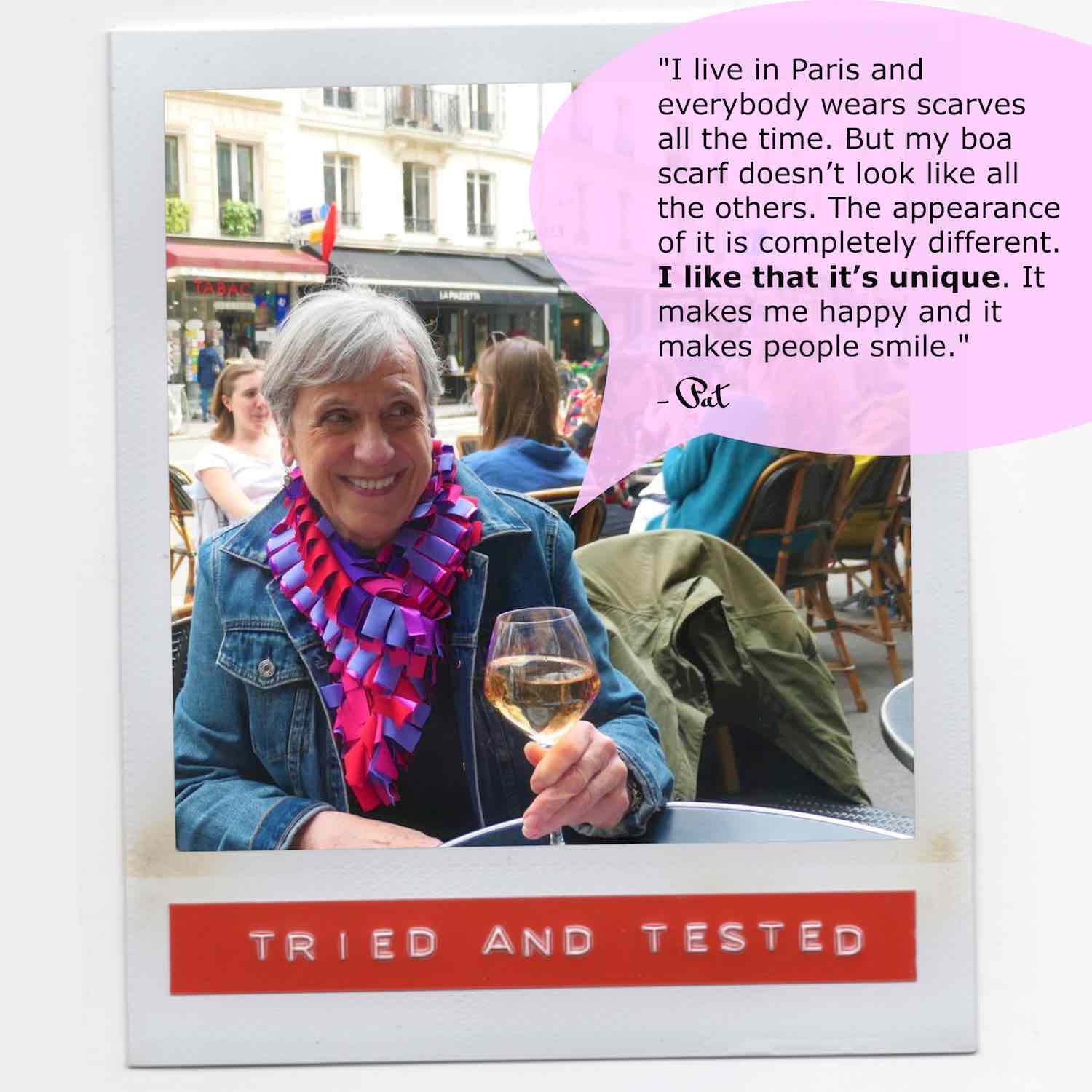 Pat smiling and wearing her multicolor fashion boa scarf with style while having a glass of wine in a Paris cafe.