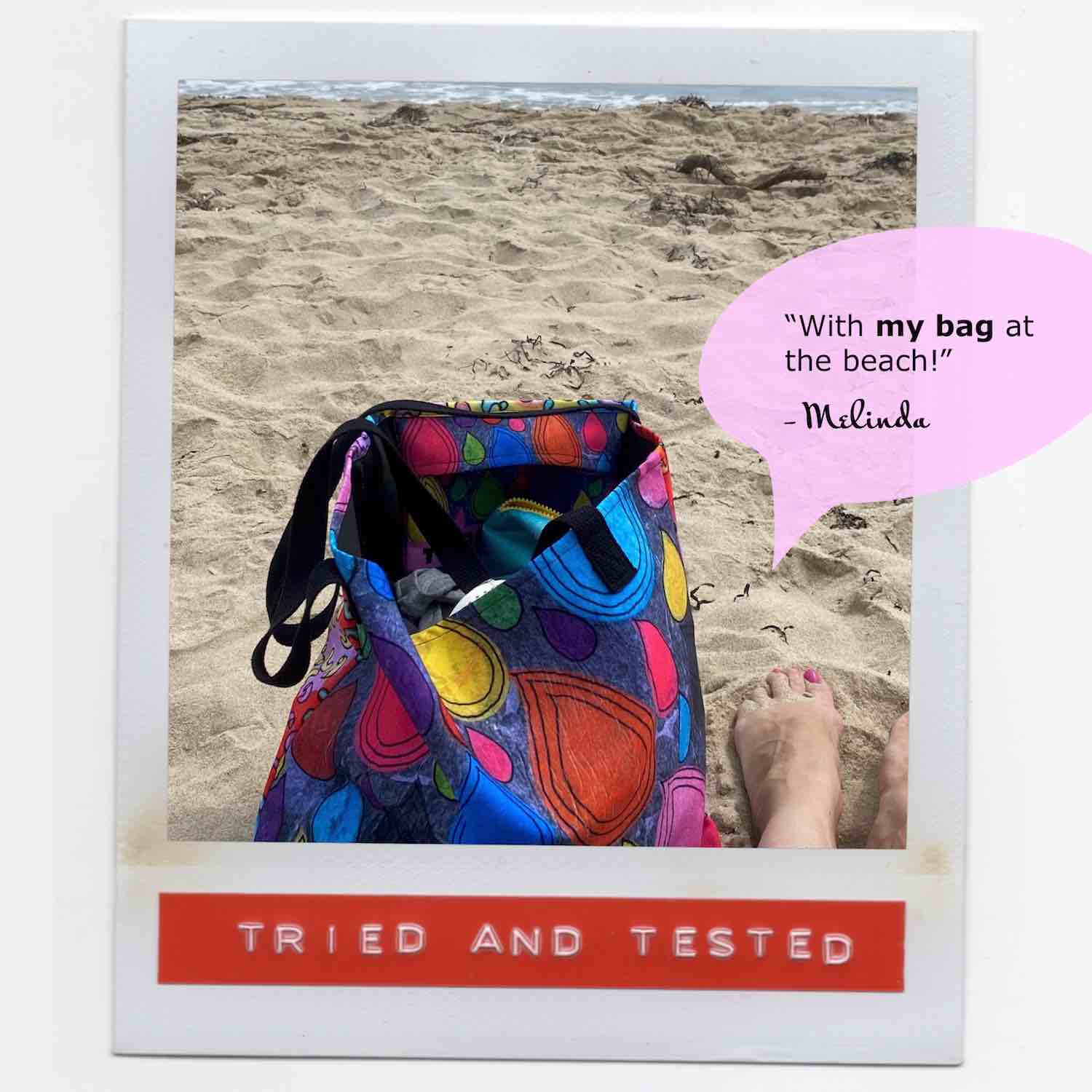 Melinda sitting on the beach with her multicolor tote bag in the sand next to her painted toenails.