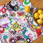 Arty graphic placemat set on wood table with happy multicolor Treasure Map print in a vibrant, cheerful, and playful style, with lemons in bowl.