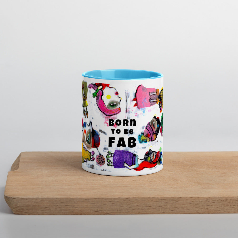 Graphic coffee mug with slogan Born To Be Fab and blue accent color on rim and interior on wood counter front view.