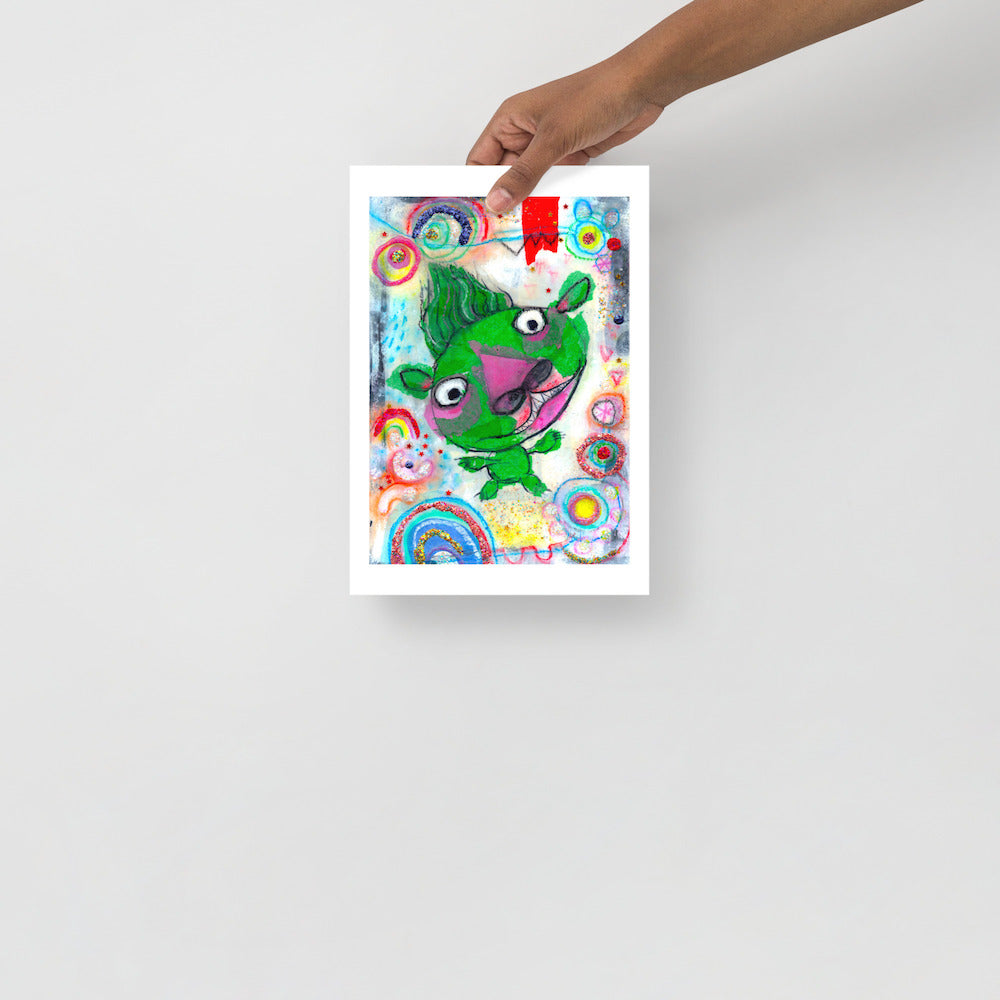 Colorful happy fine art print of a green monster smiling on vibrant background hand held against wall to show size.