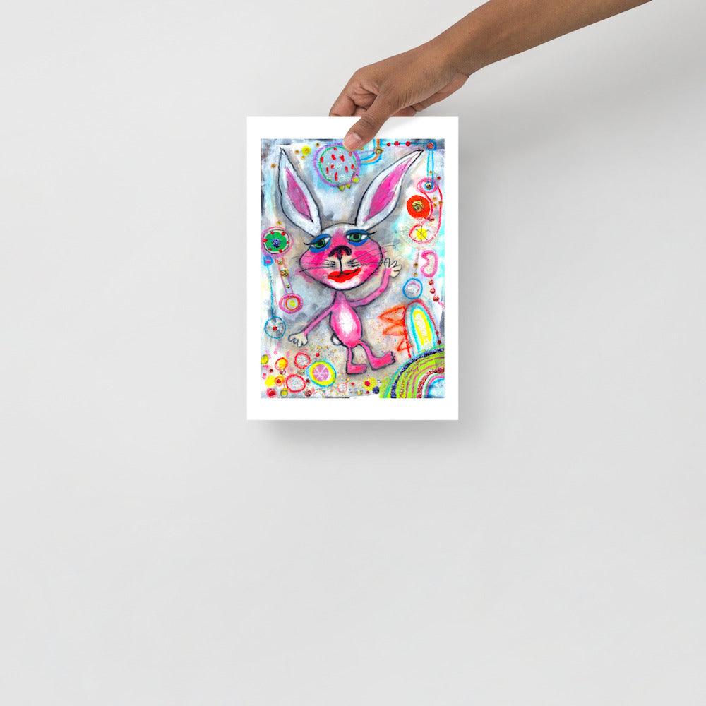 Colorful happy fine art print of a pink rabbit waving hello on vibrant background hand held against wall to show size.